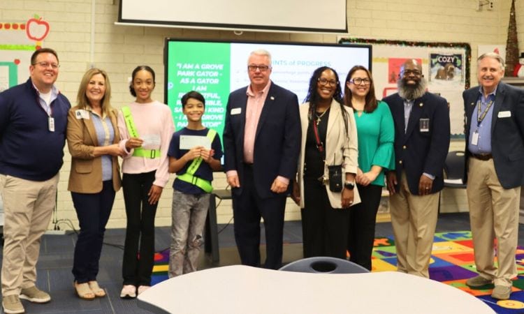 A group of 9 adults and students line up inside a school media center for a check presentation.