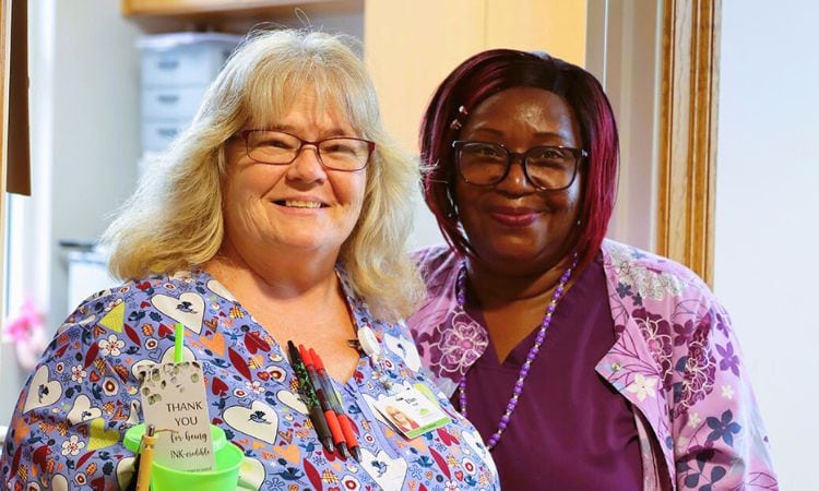 Two nurses smile and hold a small gift of appreciation